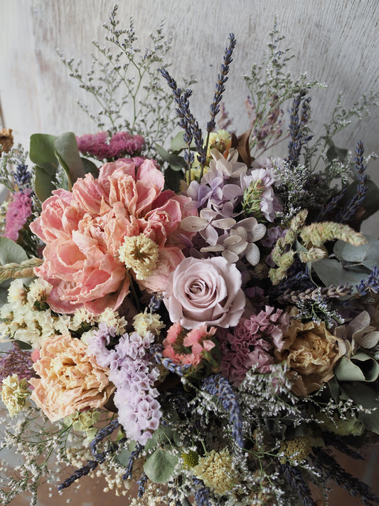 The Misty Morning Bouquet is a softly romantic dried arrangement in gentle pastel tones. Featuring wax-dipped peonies and a preserved rose, it is layered with carefully chosen complementary florals to create a light, airy feel.