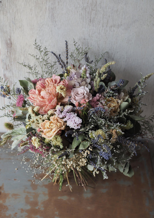 The Misty Morning Bouquet is a softly romantic dried arrangement in gentle pastel tones. Featuring wax-dipped peonies and a preserved rose, it is layered with carefully chosen complementary florals to create a light, airy feel.