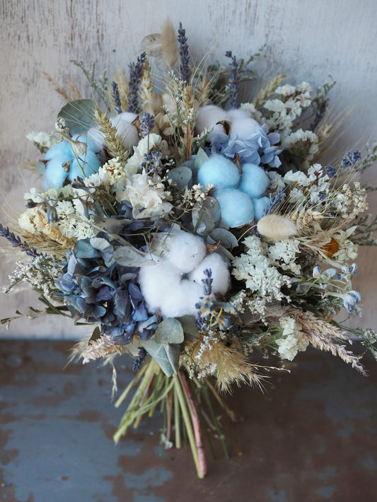 Bonny Boy Blue is a charming dried and preserved arrangement in soft blues and gentle neutrals, featuring fluffy cotton for a delicate, tender touch. Perfect for welcoming a new little bundle, celebrating a gender reveal, or adding a sweet accent to any special occasion.

Approximately 23 cm in diameter.