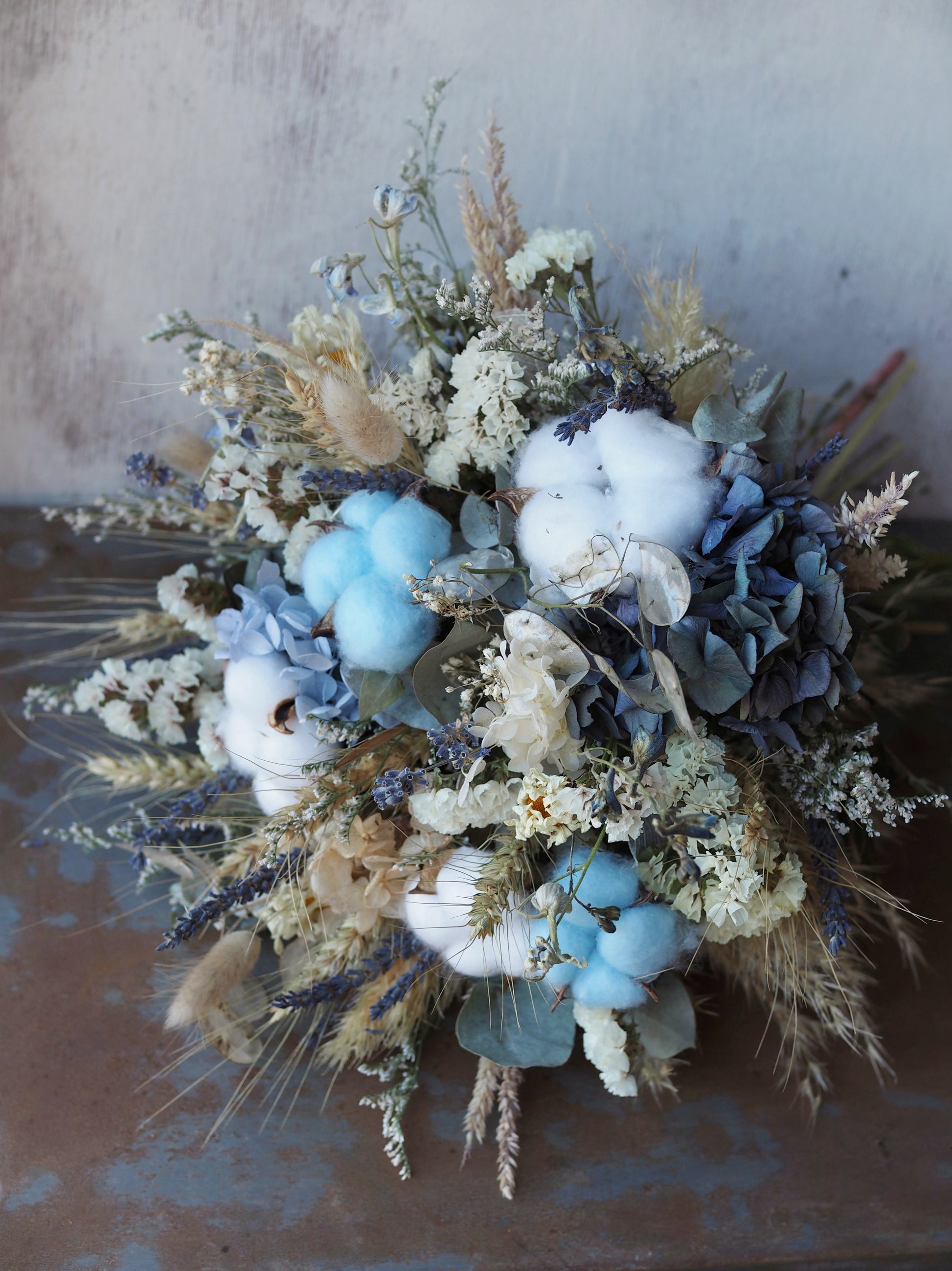 Bonny Boy Blue is a charming dried and preserved arrangement in soft blues and gentle neutrals, featuring fluffy cotton for a delicate, tender touch. Perfect for welcoming a new little bundle, celebrating a gender reveal, or adding a sweet accent to any special occasion.

Approximately 23 cm in diameter.