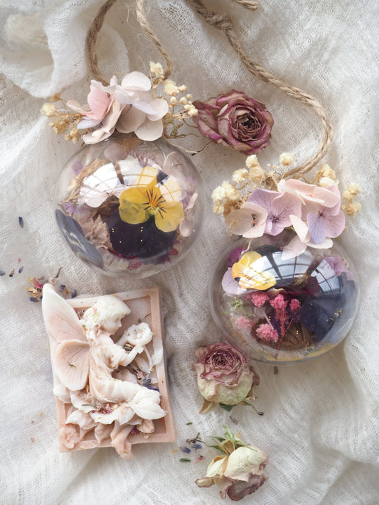 Decorative baubles spheres with dried flowers inside them and fairy soap on a soft fabric background 