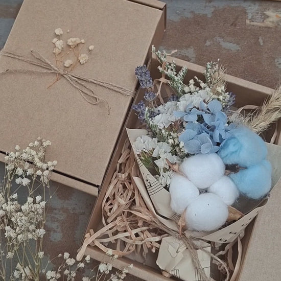 A teeny, ready-to-gift mini bouquet—just perfect for congratulations or a sweet gender reveal moment. Featuring pink or blue cotton snuggled amongst a playful mix of dried florals, each bouquet is wrapped in vintage music sheets for a touch of whimsy. Nestled inside a neutral kraft gift box to keep the colour a secret until the big surprise (Box 15 × 11.2 × 5.6 cm).